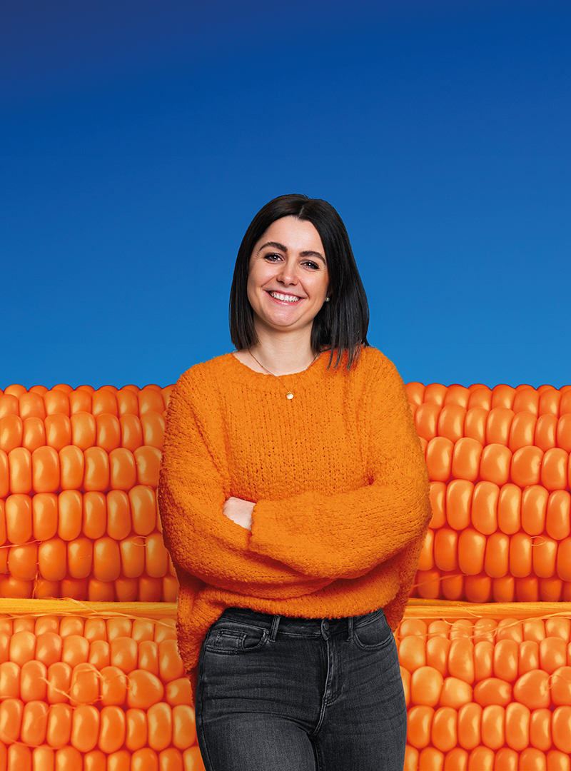 Eine sympathische, lächelnde, junge Frau vor einem blau/orangefarbenen Hintergrund.